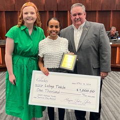 Mayor presenting oversized check in City Council chambers to a female high school student that won the 2024 National Youth Service Day Awards $1,000 scholarship.